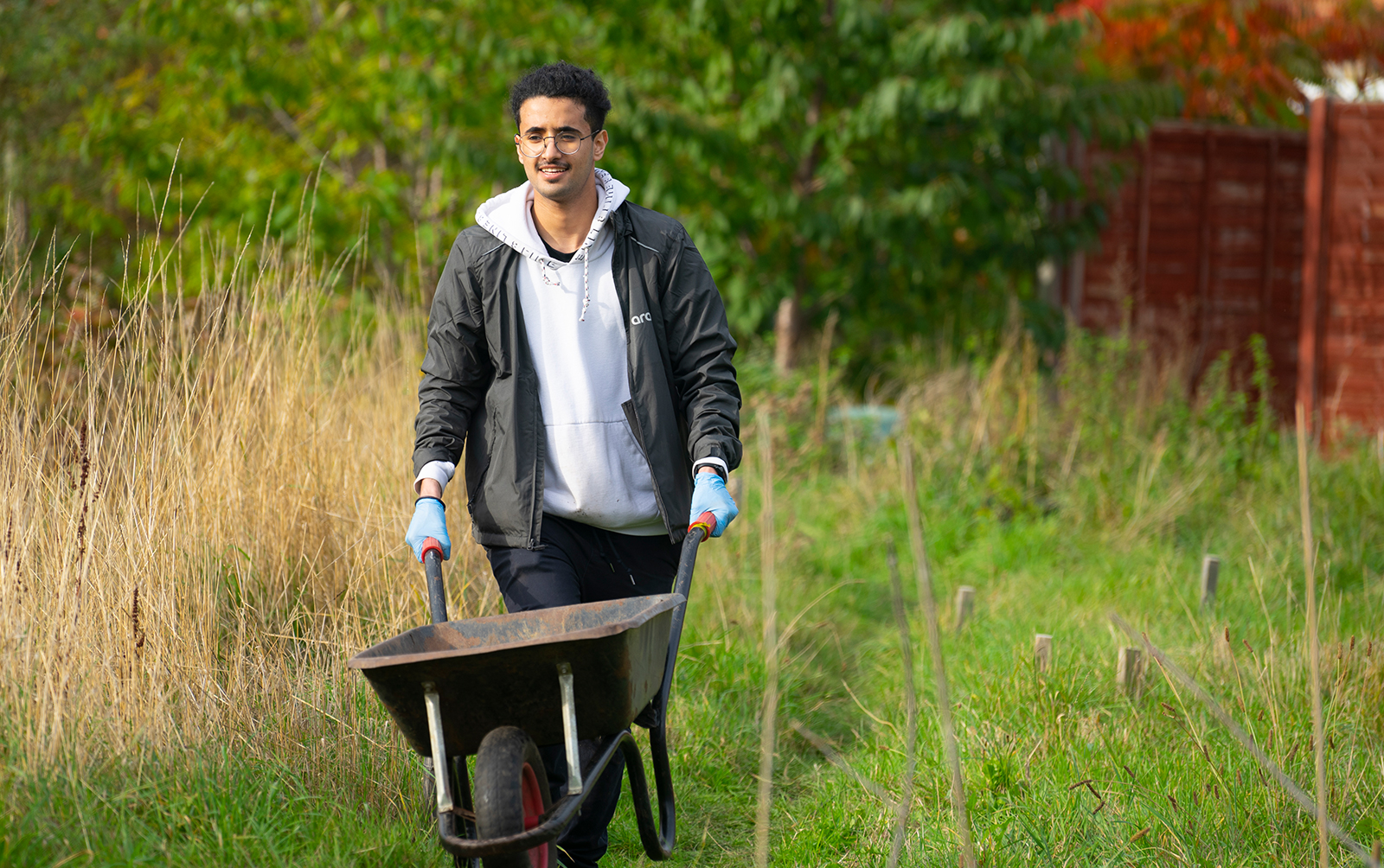 Aramco-sponsored student pushing a wheelbarrow through a community project in Lewisham, London.