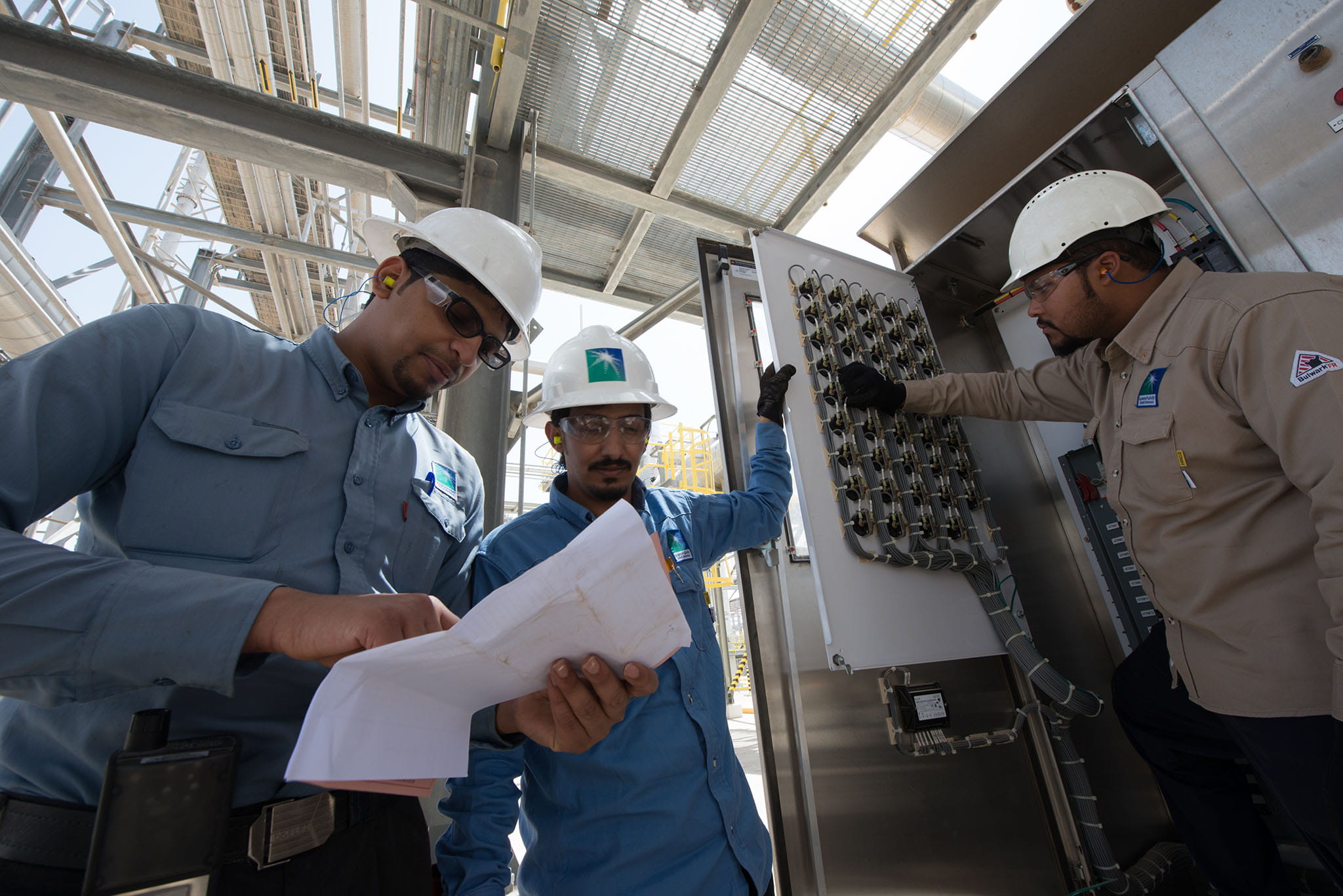 Three male Saudi Aramco workers inspect facility at Hawiyah