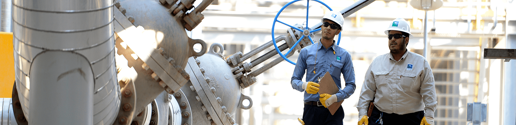 Two male Saudi Aramco employees in safety gear inspect a facility. 